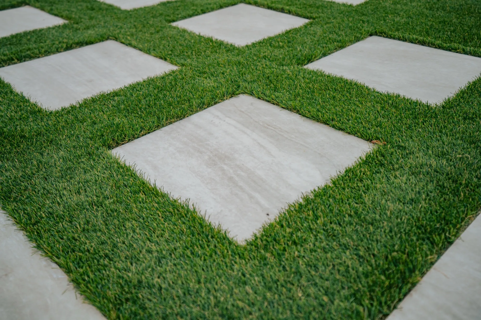 Close-up of square concrete pavers set in artificial turf in a diamond pattern